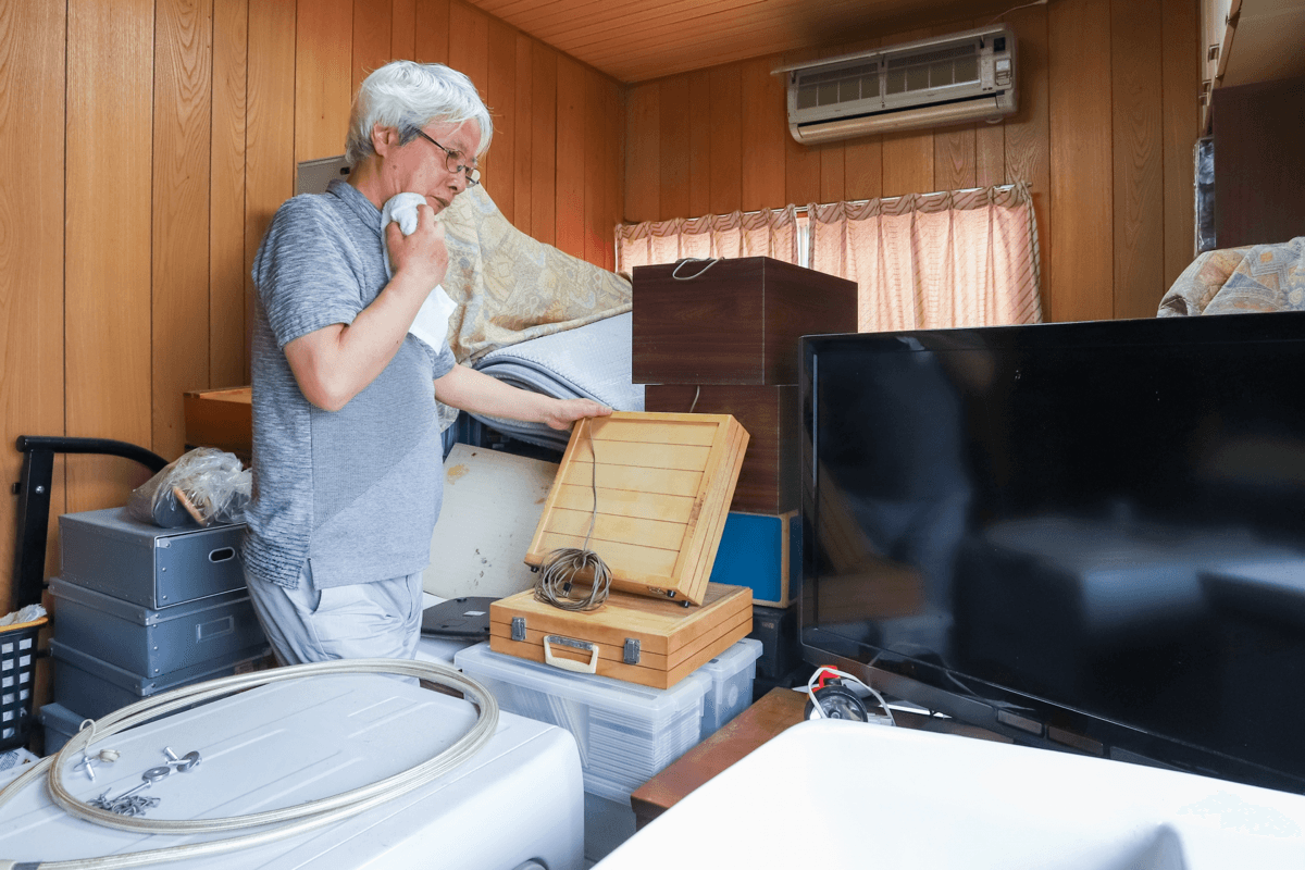 荷物に囲まれた部屋で自分で遺品整理を行っている様子